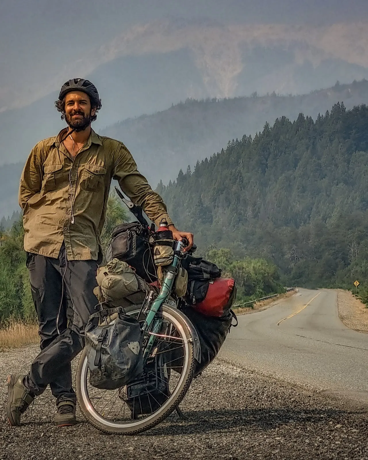 Beto Ambrósio ao lado da bicicleta carregada, em uma estrada de montanha